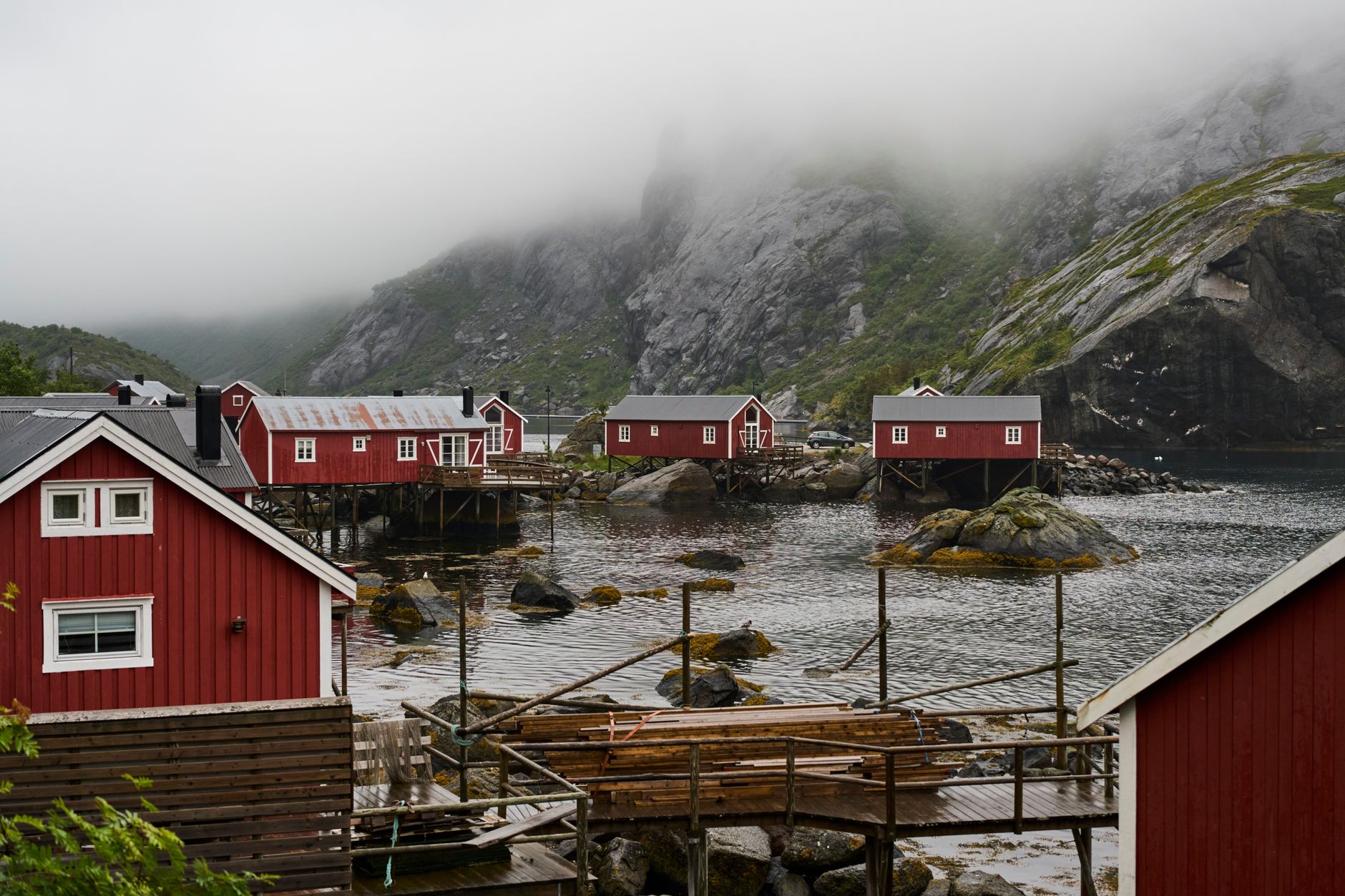 Red and ochre wooden stilt houses on rocky shoreline beneath cold morning mist
